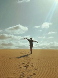 Full length of woman with arms outstretched while standing at desert against sky