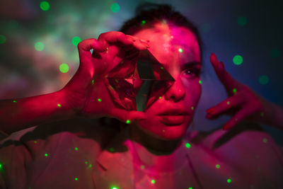 Close-up young woman looking through crystal against illuminated background