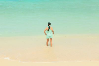Full length rear view of shirtless young woman standing on beach