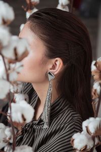 Close portrait of unrecognizable woman with earring  with cotton flower heads as background 