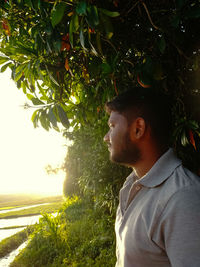 Portrait of young man looking away against trees