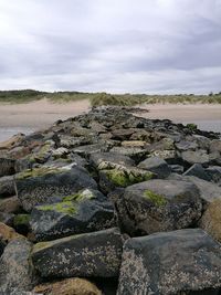 Rock groyne at seashore against cloudy sky