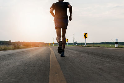 Low section of man jogging on road against sky