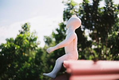 Side view of woman sitting by statue against trees