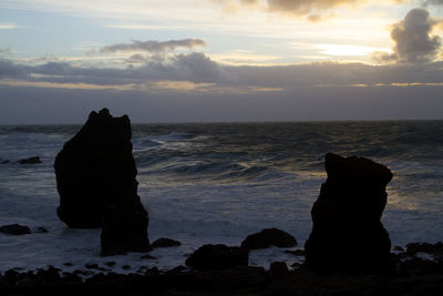 Silhouette rocks on beach against sky during sunset