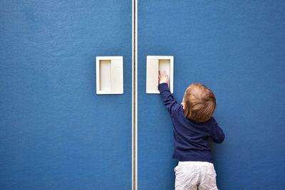 Rear view of boy standing against blue wall