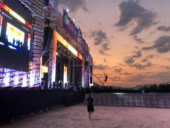 Man walking on illuminated city against sky at sunset