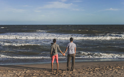 Rear view of friends standing on shore at beach