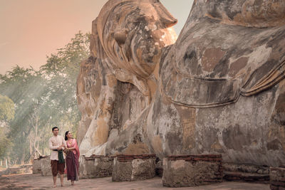 Couple wearing traditional clothing standing by statue