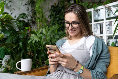 Smiling woman using smart phone sitting at home