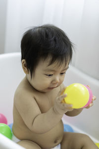 Cute baby girl holding balls in bathtub
