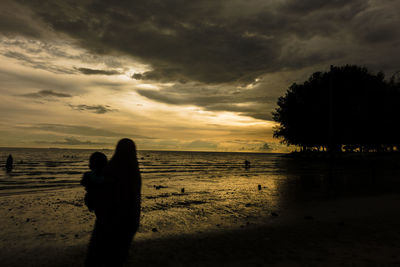 Silhouette people on beach against sky during sunset