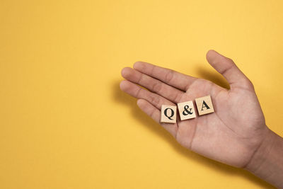 Close-up of hand holding text against yellow background