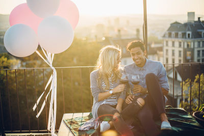 Couple sitting with wine by balloons against sky