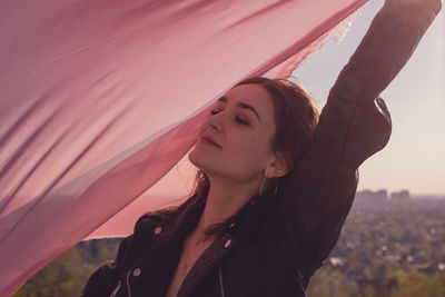 Young woman with pink scarf standing against sky during sunset