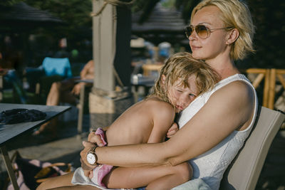 Smiling woman with daughter relaxing on chair at hotel