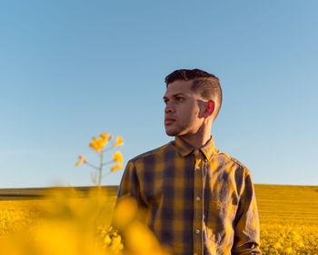 Young man looking away on field against clear sky