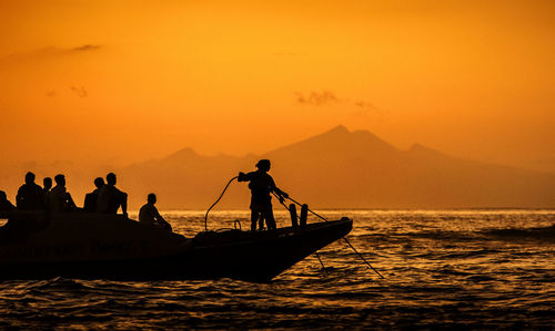 Silhouette people in boat on sea during sunset