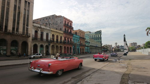 Cars on street by buildings against sky in city