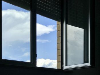 Low angle view of open window and cloud sky