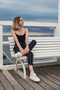 Young woman sitting on bench on wooden pier blurred beachside background. attractive female enjoying