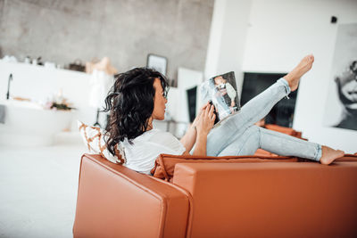 Woman reading magazine sitting on sofa at home