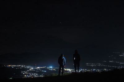 Rear view of friends standing on land against sky at night