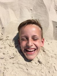 Portrait of boy buried up to his neck in sand on beach