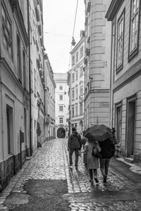 Rear view of people walking on wet street amidst buildings during rainy season