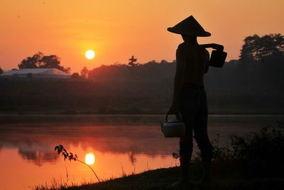 Silhouette man standing by lake against orange sky