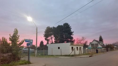 Houses and trees on field by road against sky