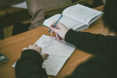 Midsection of woman writing in book on table