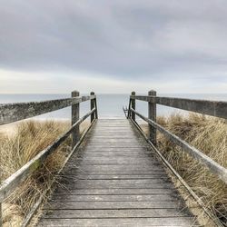 Boardwalk leading towards sea against sky