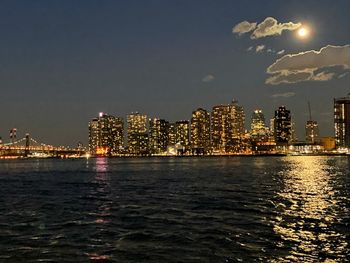 Illuminated city by sea against sky at night