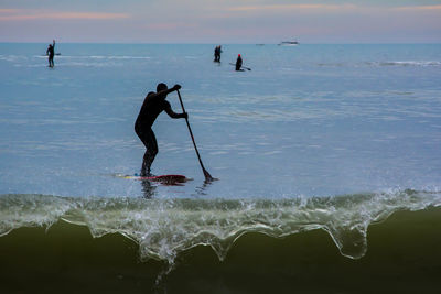 Silhouette mid adult man paddleboarding on sea against cloudy sky during sunset