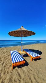 Deck chairs on beach against clear blue sky