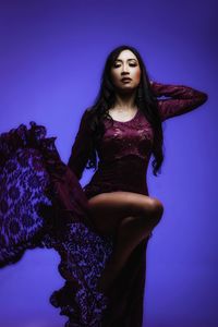 Portrait of beautiful young woman wearing dress against purple background