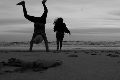 Rear view of friends enjoying on beach against sky