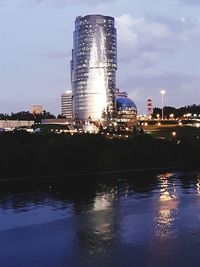 Illuminated buildings by river against sky at night