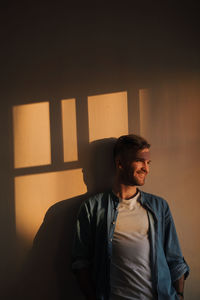 Man looking away while standing against wall