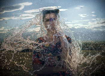 Water splashing on woman standing against sky