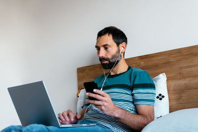 Young man using mobile phone while sitting on bed at home