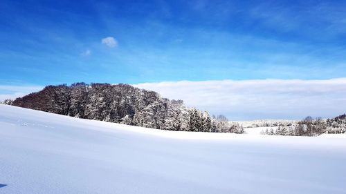 Snow covered landscape against blue sky