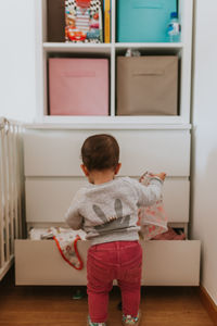 Rear view of baby boy removing clothes from drawer at home