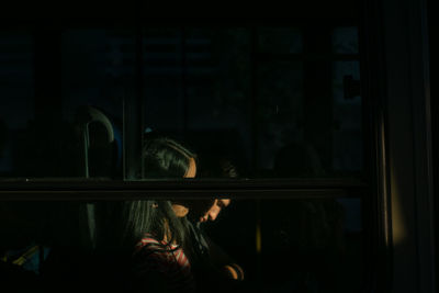 Side view of woman looking through window at home