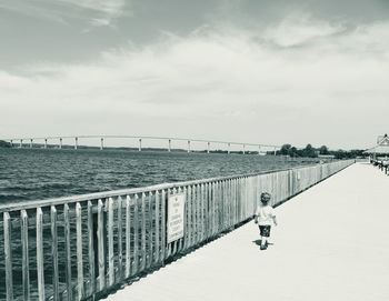 Man standing on railing by sea against sky