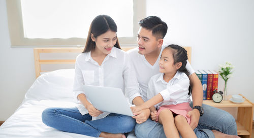 Friends using laptop while sitting on bed at home