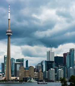 Communications tower in city against cloudy sky