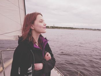 Young woman looking away while standing by sea against sky