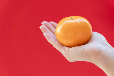 Close-up of hand holding apple against orange background